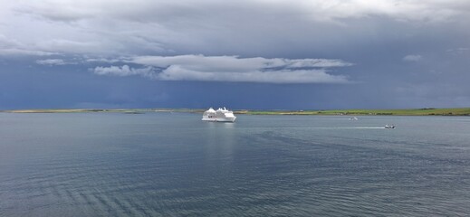kirkwall united kingdom aug 9 202 Cruise Ship Sailing Under Stormy Sky Near Scenic Green Coastline