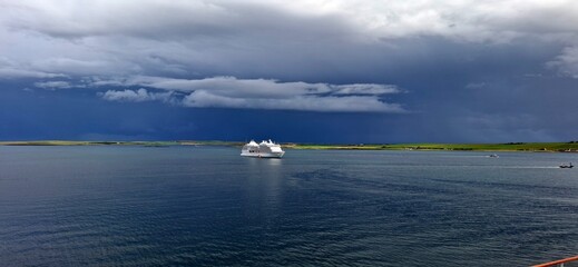 kirkwall united kingdom aug 9 202 Cruise Ship Sailing Under Stormy Sky Near Scenic Green Coastline
