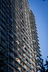 High-rise building under construction with scaffolding against a bright blue sky during the day