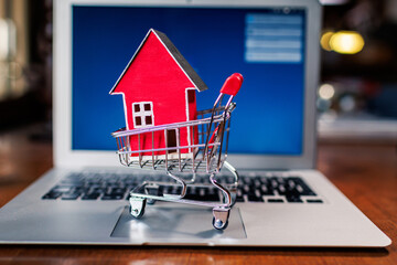miniature red house in a shopping cart on a laptop keyboard promoting online real estate shopping
