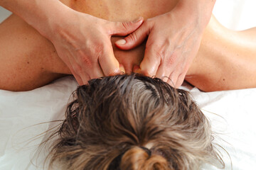  Close-up view of a professional therapist performing a neck massage on a client lying face down,...