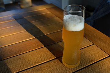 A refreshing glass of light beer with a foamy head, sitting on a wooden table 3