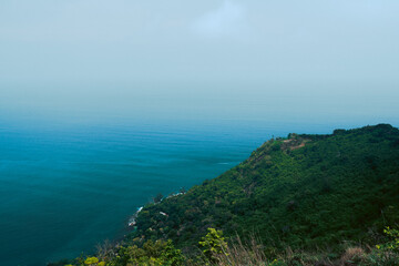 Obraz premium A serene view of a lush green headland stretching into the deep blue sea under a soft, hazy sky. The gentle gradient of ocean hues blends seamlessly with the horizon, creating a peaceful and minimalis