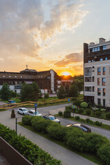 Obraz premium Modern residential neighborhood with parked cars and greenery at sunset.