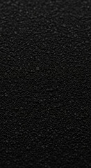 Close-up of black granular texture, showing depth and subtle variations in tone, ideal as a background for text or design elements, suggesting concepts of mystery or sophistication