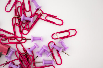 Red paper clips and purple push pins scattered on a white background, with a pink binder clip partially visible. A colorful stationery mix for office, school, and organization themes.