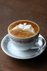 Obraz premium Coffee cup with latte art representing an open book on wooden table