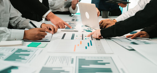 A diverse business team actively collaborating over charts and data in a modern office setting. Individuals engage with laptops, notepads, and digital tools for effective analysis. SACTR