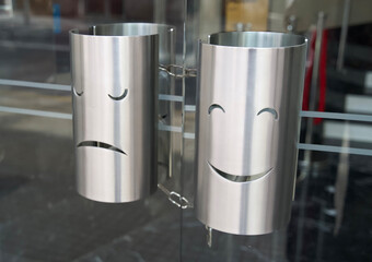 Stainless steel trash bins with smiley and sad face designs mounted on glass door for modern urban...