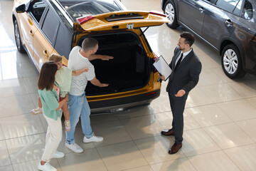Salesman with clipboard showing new car to family in salon