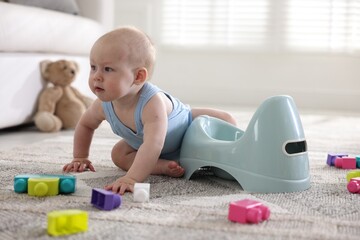 Cute little baby sitting near potty and toys at home