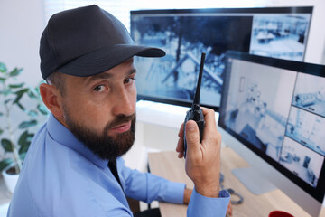 Security guard monitoring CCTV cameras and using walkie talkie in office