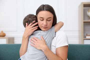 Mother supporting and hugging her sad son on sofa at home