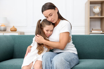 Mother supporting and hugging her sad daughter on sofa at home
