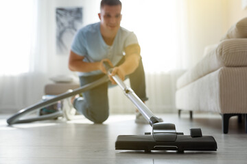 Man cleaning floor with vacuum cleaner at home, selective focus