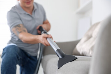 Man cleaning sofa with vacuum cleaner at home, closeup