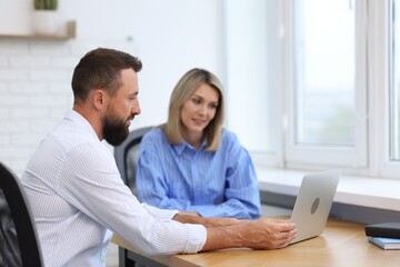 Obraz premium Smiling business partners working with laptop at table in office