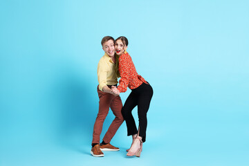 Obraz premium Happy couple in retro outfits dancing on light blue background