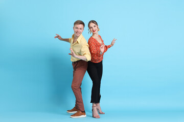 Happy couple in retro outfits dancing on light blue background
