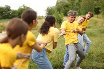 Obraz premium Team building. Group of happy people playing tug of war with rope outdoors