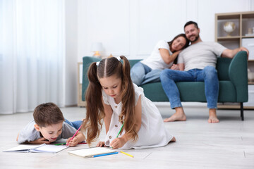 Kids drawing near their parents on warm floor at home, selective focus. Heating system