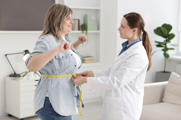 Weight loss. Nutritionist measuring happy overweight woman's waist with tape in clinic