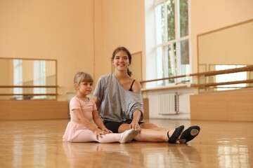 Little girl and her teacher sitting on floor in barre studio