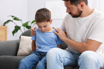 Father supporting his sad son on sofa at home