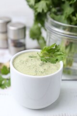 Tasty cilantro sauce in bowl on white wooden table, closeup