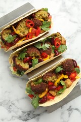Tasty vegetarian tacos with falafel, tofu, beans and vegetables on white marble table, top view