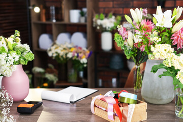 Beautiful flowers, ribbons and other tools on wooden table in florist's shop