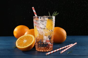 Sparkling water with orange in glass, fresh fruits and straws on blue wooden table, closeup