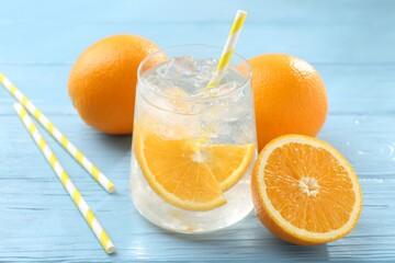 Sparkling water with orange slices in glass, fresh fruits and straws on light blue wooden table, closeup