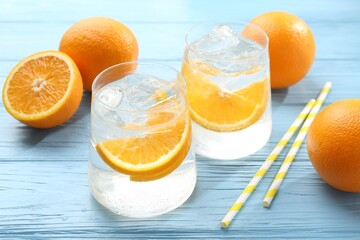 Sparkling water with orange slices in glasses, fresh fruits and straws on light blue wooden table,...