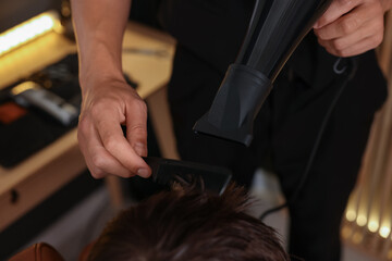 Professional barber blow drying boy's hair in barbershop, above view
