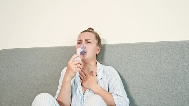 Sick woman coughing at home sitting on bed and breathing with nebulizer. Woman treating difficulty breathing with inhaler. Self-medication at home.