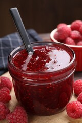 Sweet raspberry jam in glass jar and berries on table, closeup