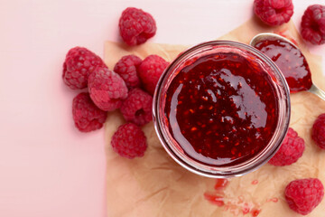 Sweet raspberry jam in glass jar and berries on pink wooden table, flat lay
