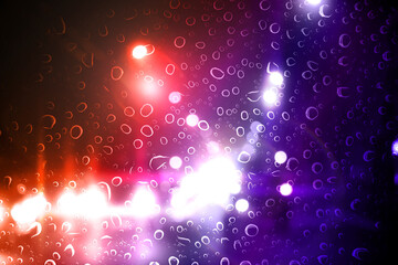 Police red and blue lights in city at night, blurred view through wet glass