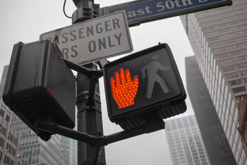 New York City pedestrian crossing signal displaying orange hand symbol with street signs and tall...