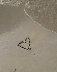 A heart drawn in wet sand waits for the gentle sea waves to erase its tender outline