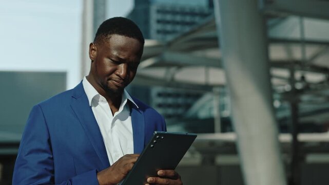 Portrait of African American man expresses concern looking at tablet in urban district. Thoughtful young trader doubted by online offer near business center. E commerce technology