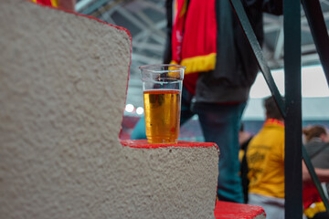 Beer on stadium seating with blurred sports fans creating atmospheric sporting event scene