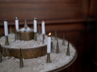 White prayer candles arranged in sand with single flame lit creating peaceful religious atmosphere