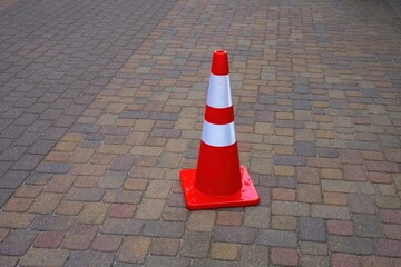 Bright orange traffic cone with white reflective stripes placed on a colorful paved surface. The...