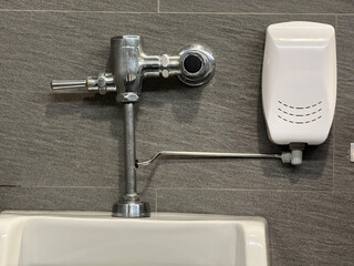Close-up of urinal flush valve and automatic air freshener on tiled wall