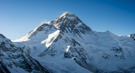 The majestic, snow-covered peak of Mount Everest is illuminated by sunlight against a clear blue sky.