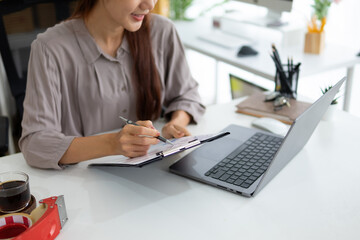 A young female entrepreneur stares at an order on her laptop screen, then she jots it down on a...