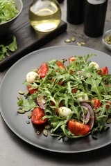 Tasty salad with arugula, mozzarella and vegetables served on grey table, closeup