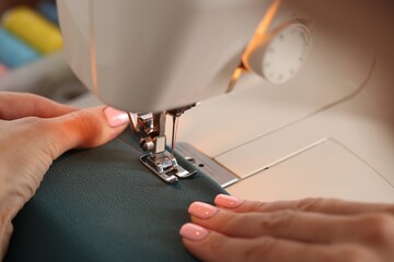 Woman working with sewing machine and fabric in workshop, closeup